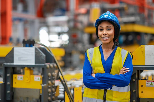 Confident female factory engineer stands with arms crossed beside industrial machinery, manufacturing professional, engineering career, leadership, workplace safety.