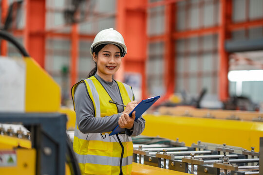 Confident female engineer smiles at camera while holding clipboard on factory floor, industrial engineering, manufacturing career, workplace safety, quality control.