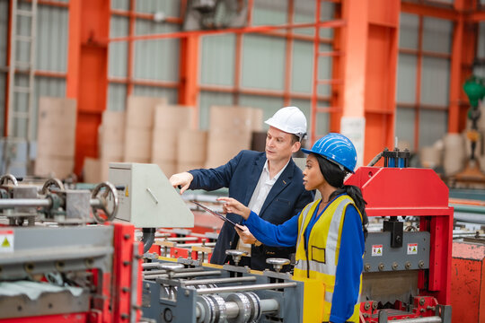 Factory manager and female engineer point at production equipment while discussing machine operation, industrial manufacturing, inspection, teamwork, quality control.