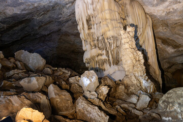 Massive stalactite formations hanging from the ceiling inside a dark limestone cavern with rocky floor © wannasak