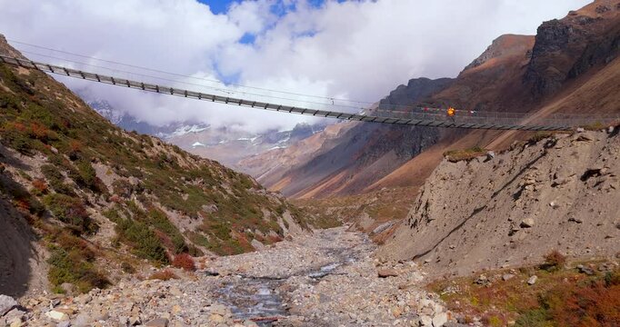 Annapurna Circuit, Manang, Nepal, gliding drone shot of a high suspension bridge spanning a mountain gorge along the trekking route to Thorong La Pass beneath Himalayan peaks.