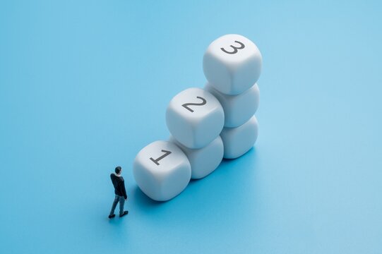 Businessman figurine looking up at a stair with numbered 1, 2, and 3 against a blue background. Step-by-step, planning, sequential career growth and business progression concept.