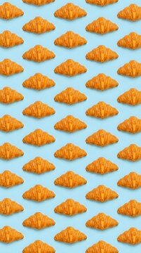 Golden croissants arranged in repeating rows on light blue