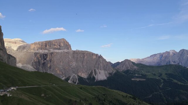 Aerial view of Sella Pass with rugged mountain peaks and green slopes under a clear blue sky in Selva, Trentino-Alto Adige, Italy.