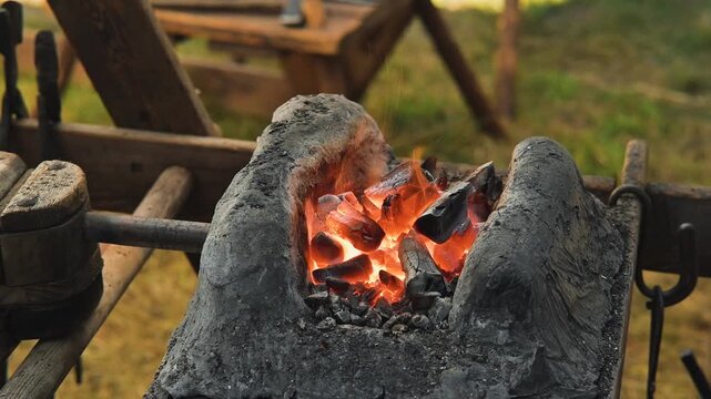 Hot coal glows brightly in a forge as a blacksmith works with metal tools. The blacksmith uses tongs to manipulate the heated metal, creating custom shapes