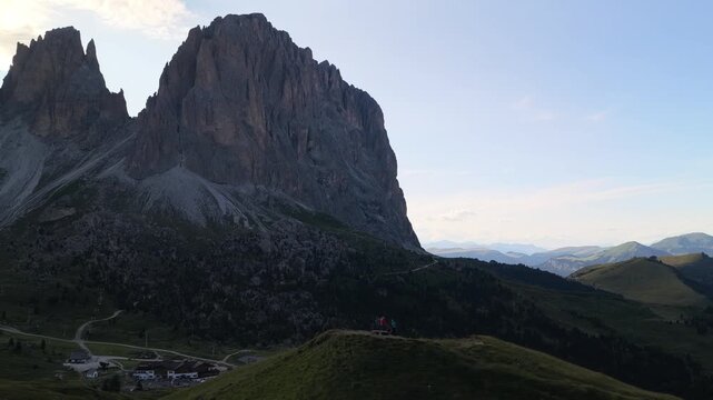 Aerial view of the dramatic limestone peaks of Sella Pass with winding mountain roads and grassy slopes in Selva, Trentino-Alto Adige, Italy.