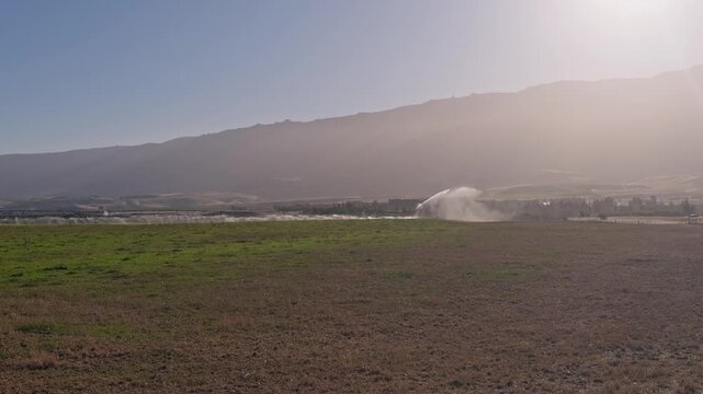Water sprays from a center pivot irrigation system across a cultivated field in a dry rural environment. Reliable irrigation helps crops thrive throughout the season.