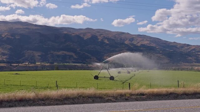 A center pivot irrigation system operates across open farmland with mountains in the distance. Wide agricultural footage showing modern water management in crop production.