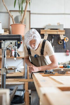 Skillful blue-collar worker working on restoration of vintage wooden door at workstation in carpentry, craftsman using tools and applying professional skills, cutting details with chisel instrument.