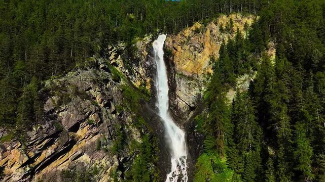 A breathtaking cinematic aerial tracking view gliding closely alongside Lehner Wasserfall as it surges over towering, jagged alpine cliffs in the picturesque &Ouml;tztal Valley.