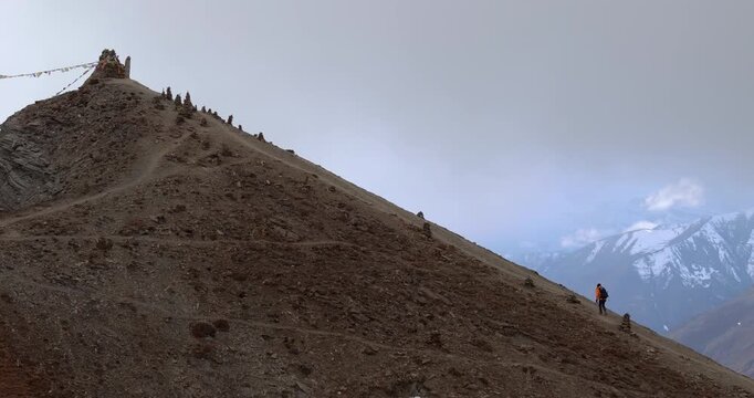 Drone push-in shot approaching a male trekker hiking up a steep rocky mountain trail along the Manang, Nepal, Annapurna Circuit route to Thorong La.