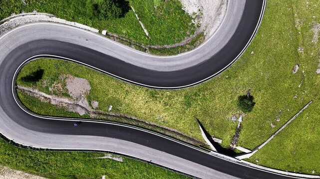Aerial view of the winding asphalt road at Passo Fedaia surrounded by lush green alpine meadows in Rocca Pietore, Veneto, Italy.