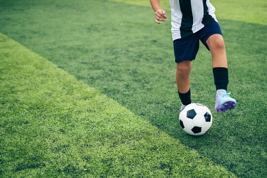 Kid boy leg kicking soccer ball on green grass field action. conceptual metaphor for youth sports training team competition fitness health wellness and active lifestyle