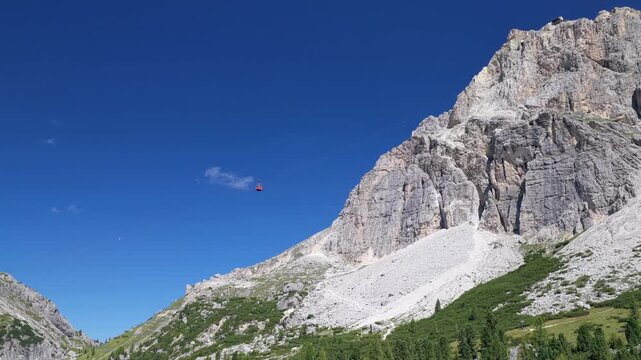 Aerial view of Passo Falzarego with a cable car crossing the rugged mountain landscape under a clear blue sky in Cortina d'Ampezzo, Veneto, Italy.