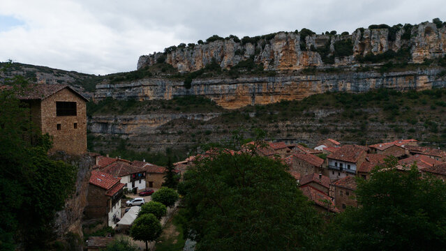 aerial view of a village nestled in lush greenery and rocky cliffs, peaceful and serene rural mountainous terrain with stone houses, Risco los camellos, Cascada de Orbaneja del Castillo