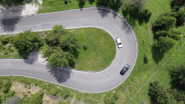 Aerial view of the winding hairpin turn at Passo Falzarego with cars driving on the mountain road surrounded by lush green forest in Cortina d'Ampezzo, Veneto, Italy.