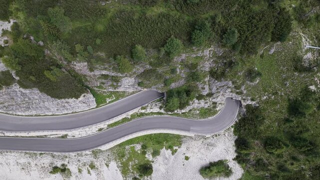 Aerial view of a car driving along the winding mountain road of Passo Falzarego surrounded by alpine slopes and rocky terrain in Cortina d'Ampezzo, Veneto, Italy.