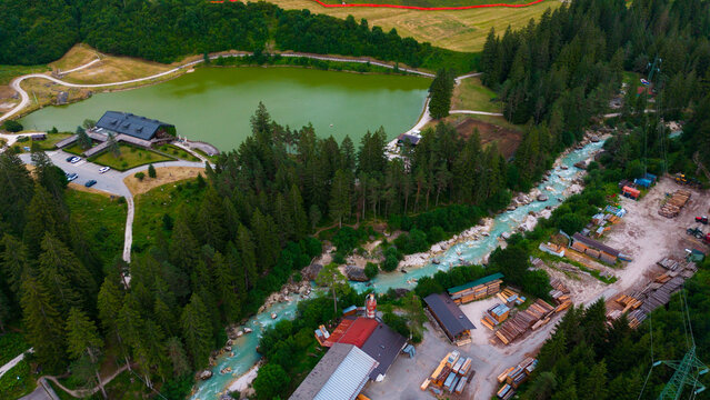 aerial view of a village with river and buildings in neutral calm setting from above with concrete, wood, and metal materials and green, brown, blue, and red colors.