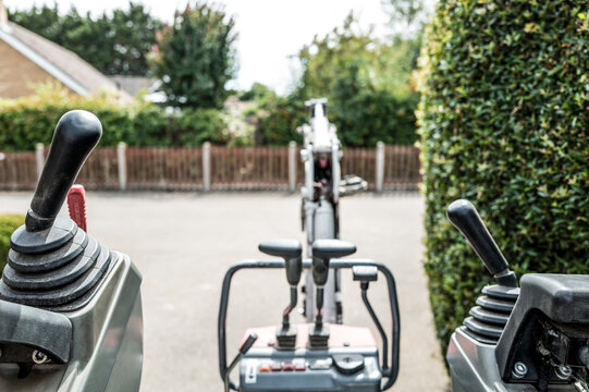 Unusual, drivers view of a small mechanical digger and excavator seen on a housing estate in the UK. The joysticks control the steering and the central levers control the hydraulic arm and scoop.