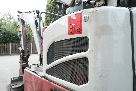 Shallow focus of the engine bay and loud noise warning sticker of a digger and excavator seen on a housing development site. The front arm and bucket can be seen.