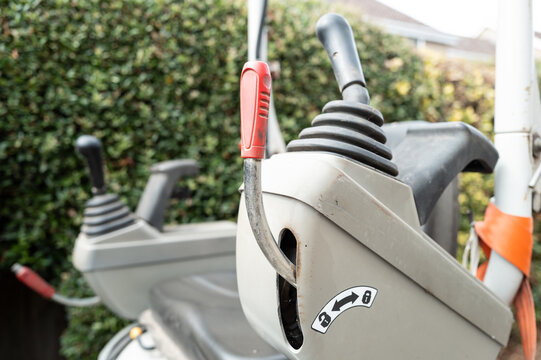 Shallow focus of the left hand steering joystick of a compact mechanical digger and excavator seen on a housing development in the UK. The red handle is for the controls to be lifted to allow access.