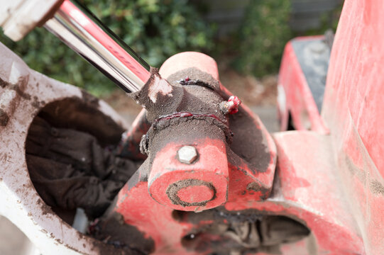 Interesting, close-up view of a greased pivot joint and hydraulic piston seen on a mini digger and excavator. The excavator is about to undergo a hydraulic service.