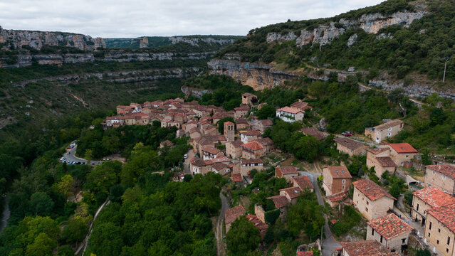peaceful aerial view of a small village nestled within forested hills in rural, mountainous terrain with red-tiled roofs and stone buildings, Risco los camellos, Cascada de Orbaneja del Castillo