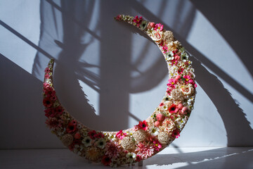 A large crescent moon sculpture decorated with vibrant pink and white flowers © wundermann