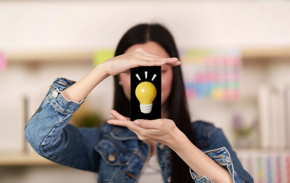 Woman holding smartphone with glowing lightbulb screen for creative idea concept