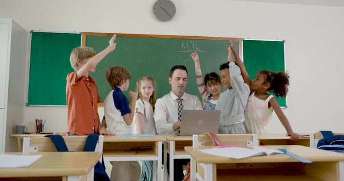 Young multicultural pupil group raises hand around male adult teacher during back to school classroom question time, creating primary lesson engagement, confidence, teamwork and positive discipline