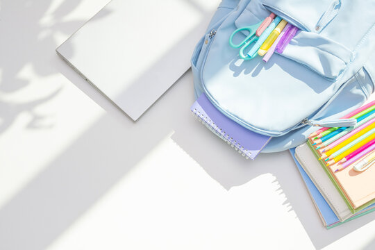 Blue backpack, laptop and school supplies top view on white table in light and shadow background