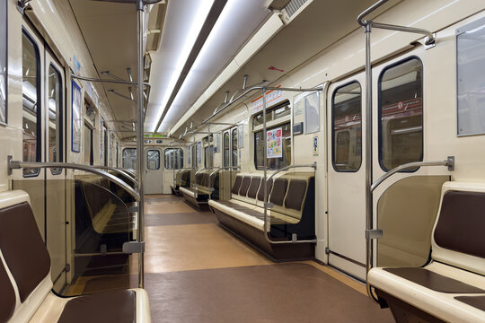 Interior of a subway train featuring brown and cream seating with metal handrails, illuminated by bright overhead lights, creating a spacious and clean environment for commuters