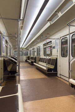 Interior of a empty subway train featuring brown and cream seating with metal handrails, illuminated by bright overhead lights, creating a spacious and clean environment for commuters