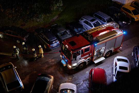 Firefighters professionals and fire truck during nighttime emergency response in heavy rain. Fire service operations, public safety, disaster response, emergency preparedness, first responder activity