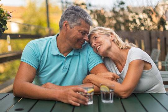 Laughing mature couple leaning close at an outdoor table