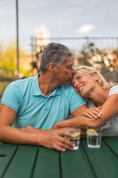 Man kissing a woman's forehead at an outdoor table