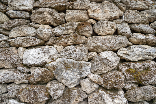 A rustic dry stone wall built from rough limestone boulders with patches of moss shows a traditional masonry technique. The uneven surface creates a natural rugged background texture.