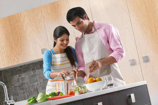 Young couple preparing vegetable salad in kitchen
