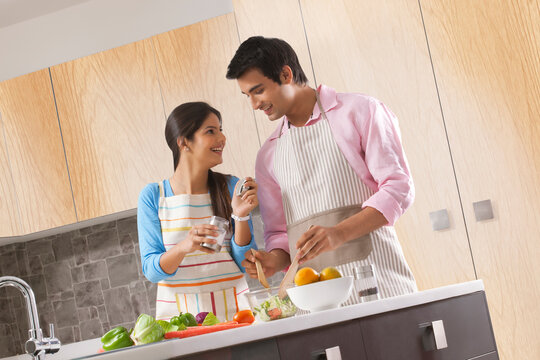 Young couple seasoning fresh salad with salt in kitchen