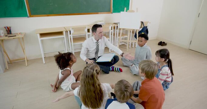 High angle classroom view follows male adult teacher guiding young multicultural pupil circle on floor, leading first day lesson routine, question time, participation, teamwork and respect today