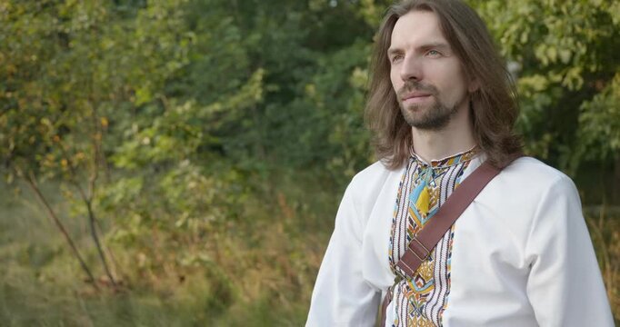 Caucasian man with long hair and Ukrainian traditional folk attire walk wandering on nature. 4K 10-bit