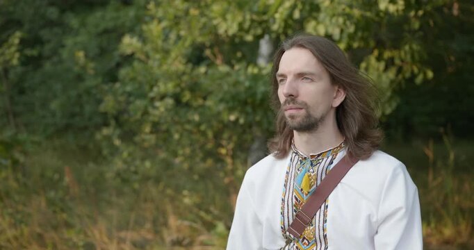Caucasian man with long hair and Ukrainian traditional folk attire walk wandering on nature. 4K 10-bit