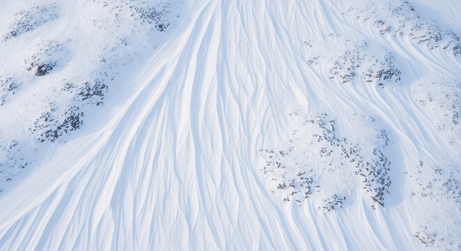 Aerial Top View of Wind-Carved Snow Textures and Sastrugi Patterns on a Frozen Mountain Slope
