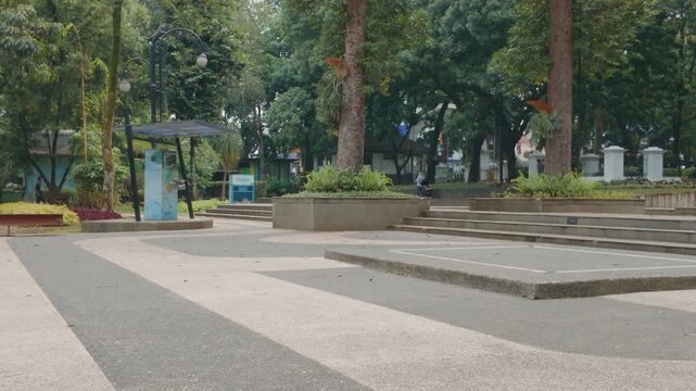 Quiet public park with stone pathways, steps, lush green trees, and flower beds during daytime.