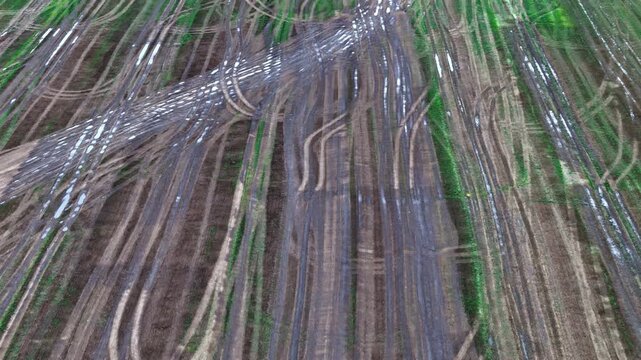 Aerial view of muddy agricultural field with deep tire tracks from heavy machinery in Latvia.