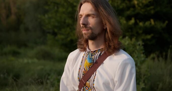 Caucasian man with long hair and Ukrainian traditional folk attire walk wandering on nature. 4K 10-bit