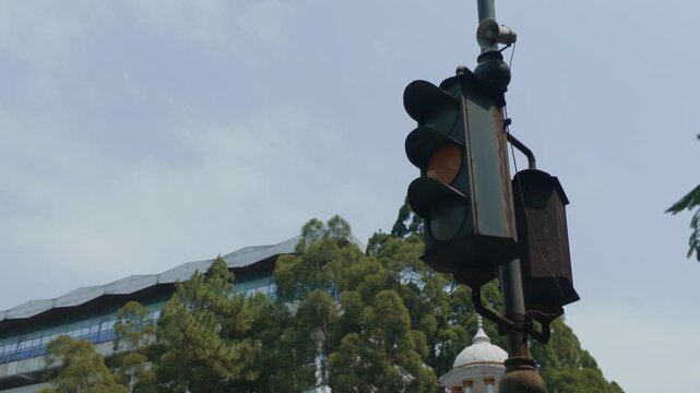 Old vintage traffic light hanging on a pole against cloudy sky and trees.
