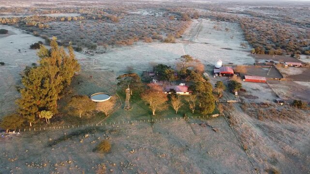 Drone perspective of early morning frost covering a South American farm as the warm sunrise hits the ground