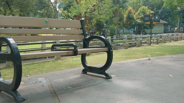 An empty wooden park bench situated along a pathway in a green public park.