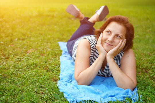 Caucasian woman lying on a blanket on grass with bent legs in brown sneakers, ideal for carefree lifestyle, casual footwear and summer leisure content.